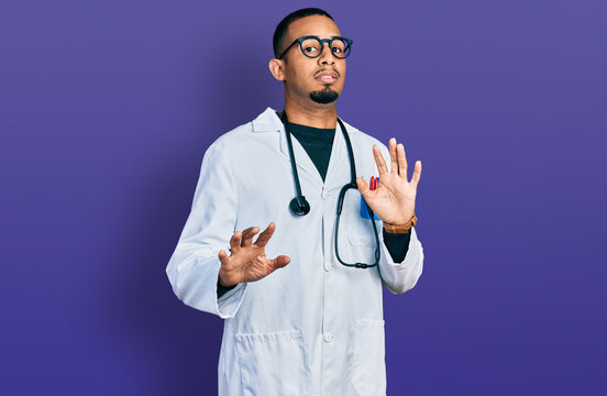 Young african american man wearing doctor uniform and stethoscope afraid and terrified with fear expression stop gesture with hands, shouting in shock. panic concept.