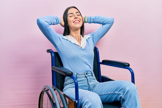 Beautiful Woman With Blue Eyes Sitting On Wheelchair Relaxing And Stretching, Arms And Hands Behind Head And Neck Smiling Happy