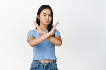 Young asian woman shows cross, stop block gesture, tell no, prohibit something bad, frowning...