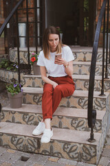 Stylish woman sitting on the steps of a building on the street and talking on the phone