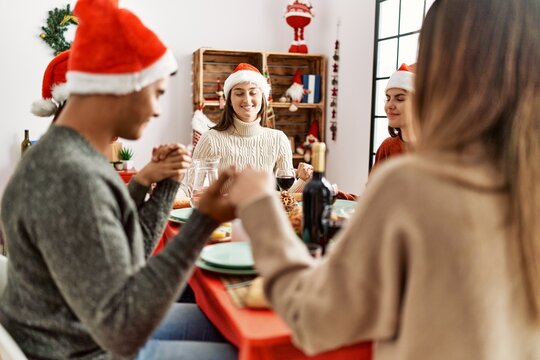 Group of young people celebrating christmas praying for food sitting on the table at home.