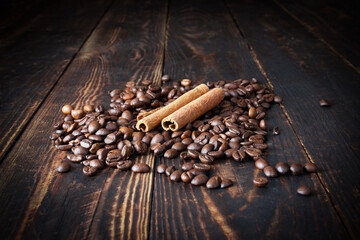 Sprinkled coffee beans and two cinnamon sticks on brown plank wooden surface
