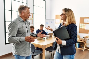 Two middle age business workers speaking while partners working at the office.