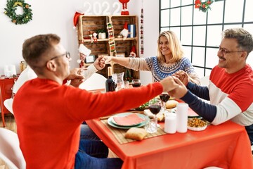 Group of middle age caucasian family having christmas dinner and praying for food sitting on the table at home.