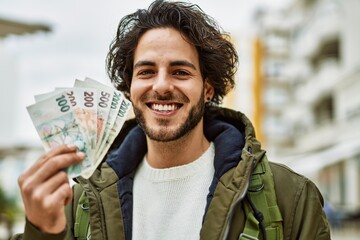 Handsome hispanic man holding czech crown banknotes at the city