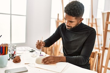 Young african american artist man concentrated painting pottery at art studio.