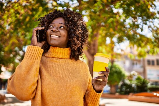 African american woman talking on the smartphone drinking coffee at park
