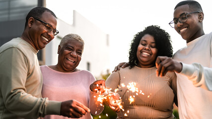 Happy African family celebrating holidays with sparklers fireworks at house party - obrazy, fototapety, plakaty