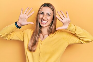 Beautiful hispanic woman wearing casual yellow sweater showing and pointing up with fingers number ten while smiling confident and happy.