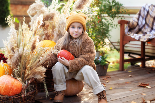 happy child with pumpkin outdoor in halloween in garden. Smiling girl sit on porch with a pumpkin in her hands. Trick-or-treat. Happy little girl playing on steps home. Child in cozy fall backyard.	
