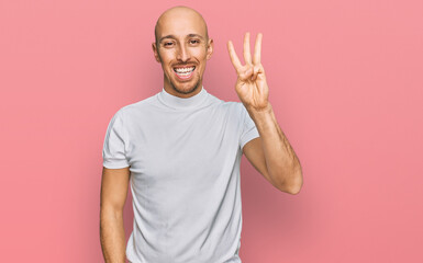 Bald man with beard wearing casual white t shirt showing and pointing up with fingers number three while smiling confident and happy.