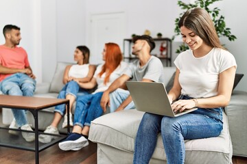 Group of young friends speaking sitting on the sofa. Woman smilimg happy and using laptop at home.