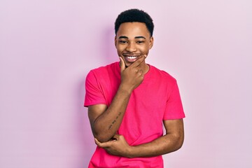 Young african american man wearing casua t shirt looking confident at the camera smiling with crossed arms and hand raised on chin. thinking positive.