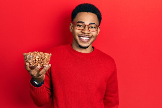 Young african american man holding peanuts looking positive and happy standing and smiling with a confident smile showing teeth