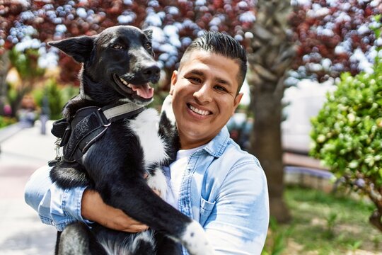 Young latin man smiling happy holding dog at the city.
