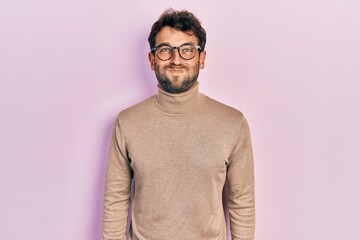 Handsome man with beard wearing turtleneck sweater and glasses puffing cheeks with funny face. mouth inflated with air, crazy expression.