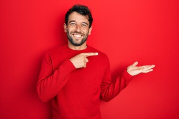 Handsome man with beard wearing casual red sweater amazed and smiling to the camera while...