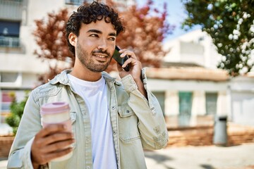 Handsome hispanic man with beard smiling happy outdoors on a sunny day having a conversation...