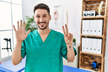 Young physiotherapist man working at pain recovery clinic showing and pointing up with fingers...