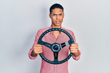 Young african american guy holding steering wheel clueless and confused expression. doubt concept.