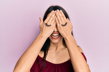 Young hispanic woman covering eyes with hands and fake lashes smiling and laughing hard out loud because funny crazy joke.