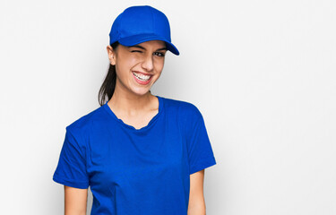 Young hispanic girl wearing delivery courier uniform winking looking at the camera with sexy expression, cheerful and happy face.