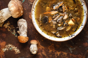 Homemade hot soup in white craft bowl with fresh wild mushrooms, potatoes, carrots and onion on...