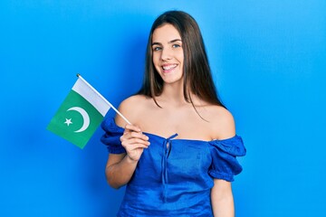 Young brunette teenager holding pakistan flag looking positive and happy standing and smiling with a confident smile showing teeth
