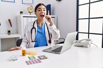 Obraz premium Young hispanic doctor woman wearing doctor uniform working at the clinic pointing finger up with successful idea. exited and happy. number one.