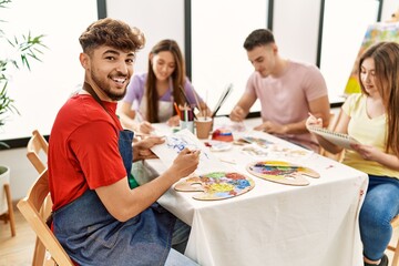 Group of people drawing sitting on the table. Young man smiling happy looking to the camera at art studio.