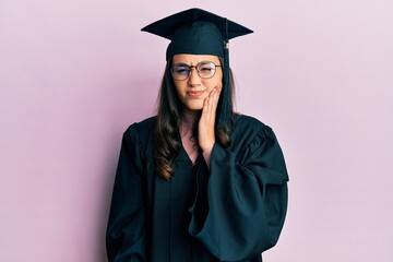 Young hispanic woman wearing graduation cap and ceremony robe touching mouth with hand with painful expression because of toothache or dental illness on teeth. dentist