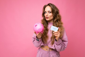 Portrait photo of happy positive young beautiful attractive woman with wavy long blonde hair with sincere emotions wearing stylish pink hoodie isolated over pink background with copy space, holds pink