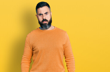 Hispanic man with beard wearing casual winter sweater in shock face, looking skeptical and...
