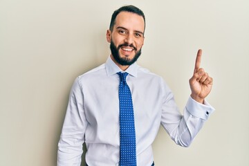 Young man with beard wearing business tie showing and pointing up with finger number one while smiling confident and happy.
