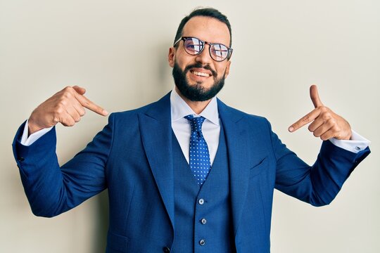 Young man with beard wearing business suit and tie looking confident with smile on face, pointing oneself with fingers proud and happy.