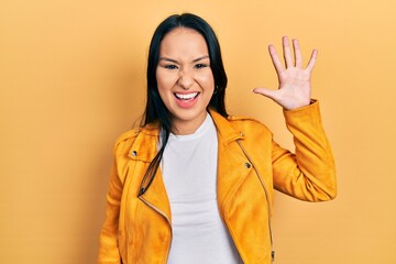 Beautiful hispanic woman with nose piercing wearing yellow leather jacket showing and pointing up...