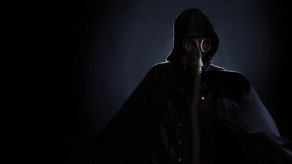 A gloomy man in dark clothes, a black hood on his head, a gas mask protects his face.