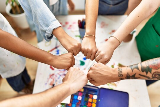 Group of people sitting on the table bump fists at art studio.