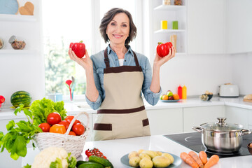 Photo of cheerful positive charming old woman hold hands peppers cook food indoors inside house home kitchen