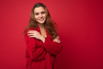 Fototapeta premium Portrait of young attractive caucasian hipster woman in trendy casual clothes. Sexy carefree female person posing isolated near red wall in studio. Positive model with natural makeup. Empty space