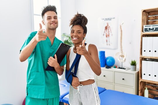 Physiotherapist working with patient wearing arm on sling at rehabilitation clinic pointing fingers to camera with happy and funny face. good energy and vibes.