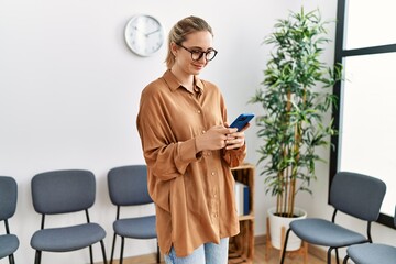 Young blonde woman smiling confident using smartphone at waiting room