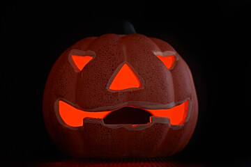 A low angle shot of a glowing carved pumpkin in a black background - halloween concept