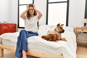 Young brunette woman sitting on the bed with two dogs suffering from headache desperate and stressed because pain and migraine. hands on head.