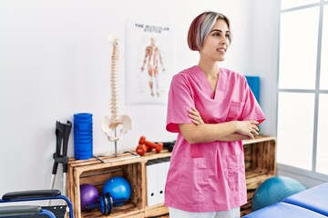 Young caucasian physiotherapist smiling happy standing with arms crossed gesture at the clinic.