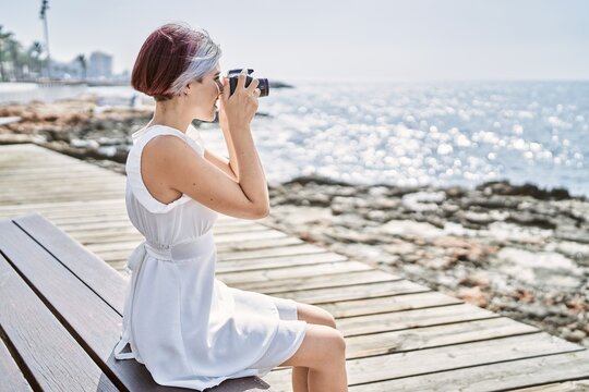 Young caucasian girl using professional camera sitting on the bench at the beach.