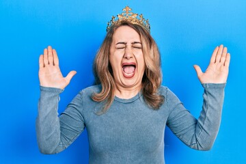 Middle age caucasian woman wearing queen crown celebrating mad and crazy for success with arms...