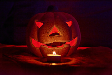 An illuminated carved pumpkin and a candle in a dark background - halloween concept