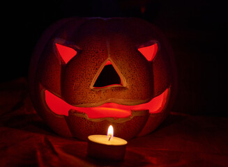 An illuminated carved pumpkin and a candle in a dark background - halloween concept
