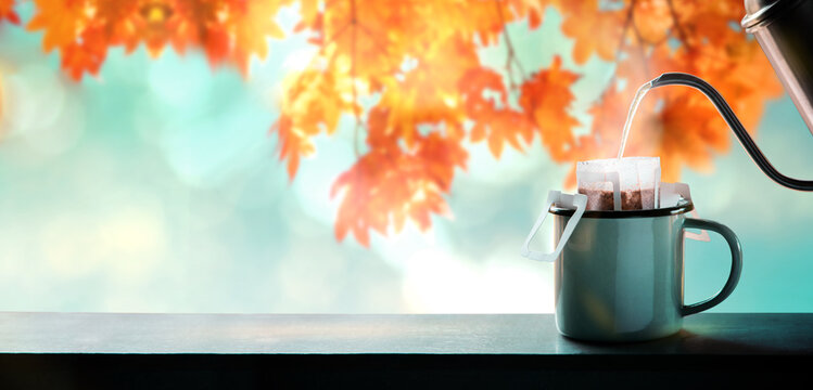 Enjoying Coffee in Fall and Autumn Season. Making Hot Coffee by Pouring Water from Kettle into an Instant Coffee Drip Bag. blurred Maple Leaf Tree as background